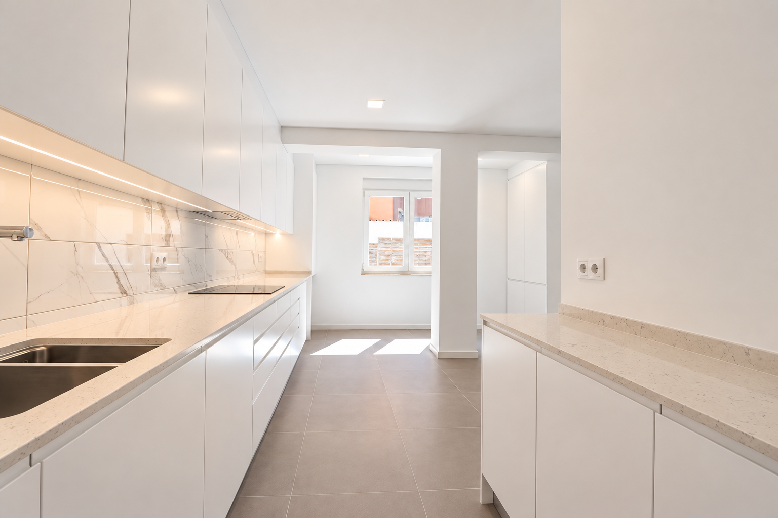 Cozinha com móveis brancos, bancadas paralelas e iluminação sob os armários.