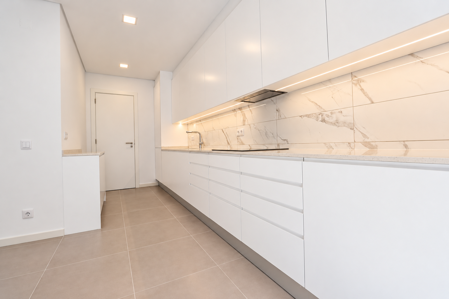 Cozinha com bancada comprida, armários brancos e porta interior ao fundo.
