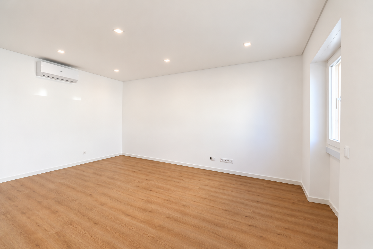 Sala clara com ar condicionado, janela lateral e pavimento em tom de madeira.