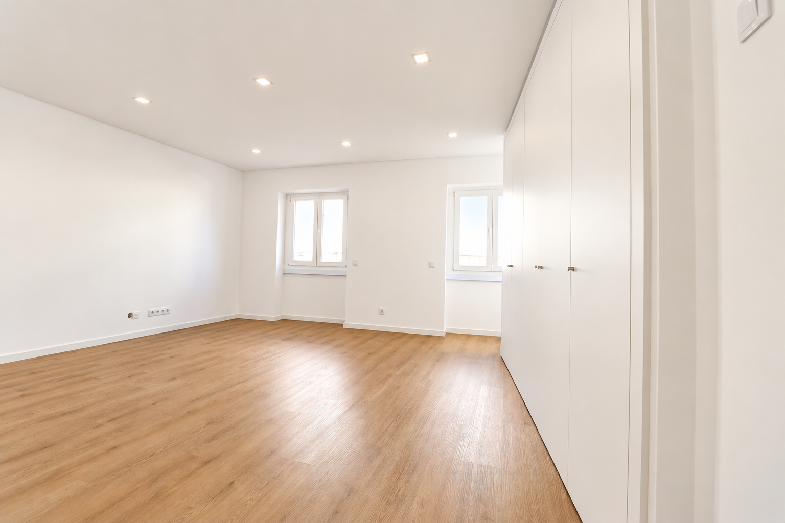 Sala com duas janelas e focos embutidos, vista junto ao grande armário branco.