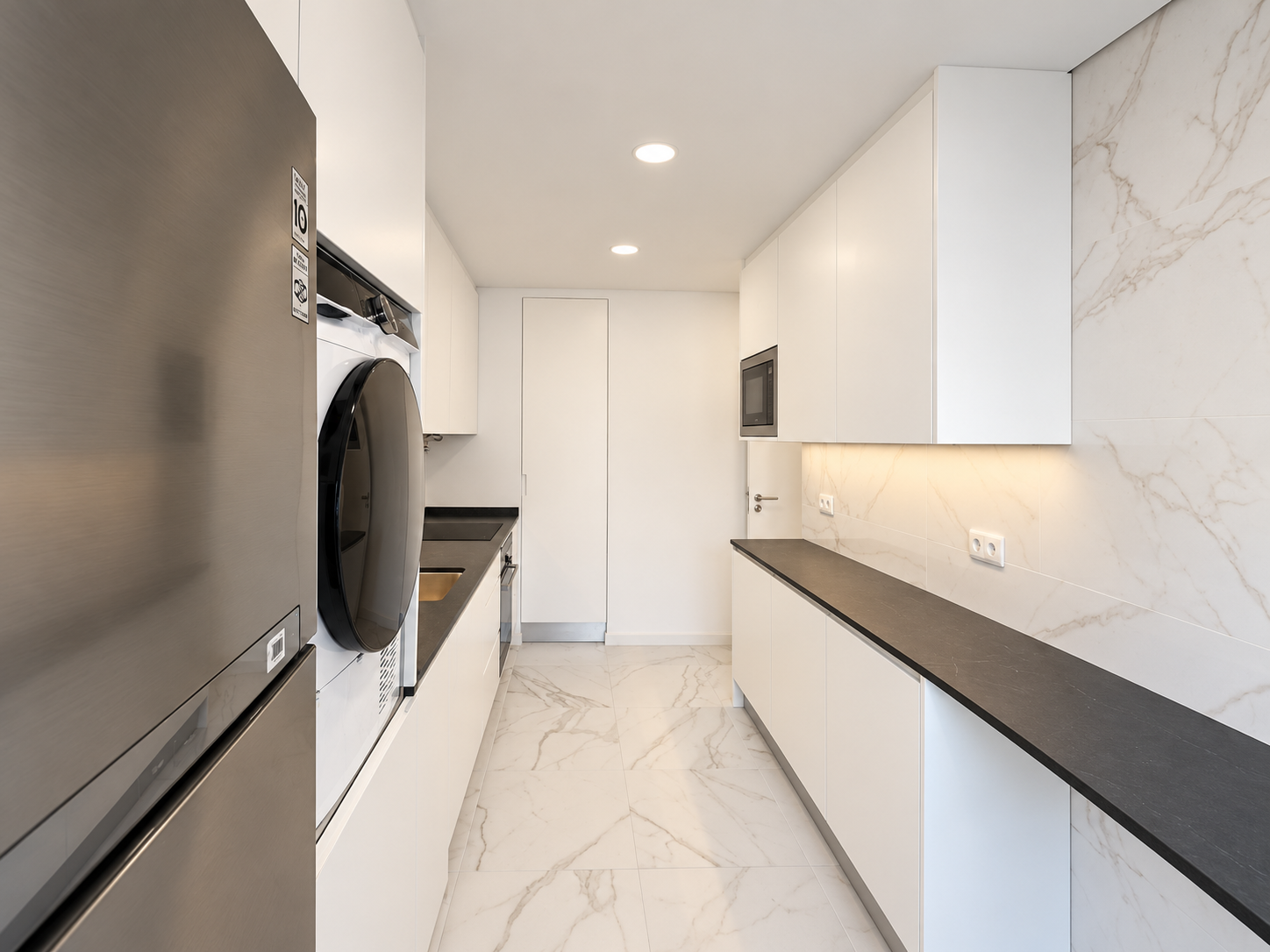 Frigorífico e eletrodomésticos em coluna junto às duas bancadas da cozinha