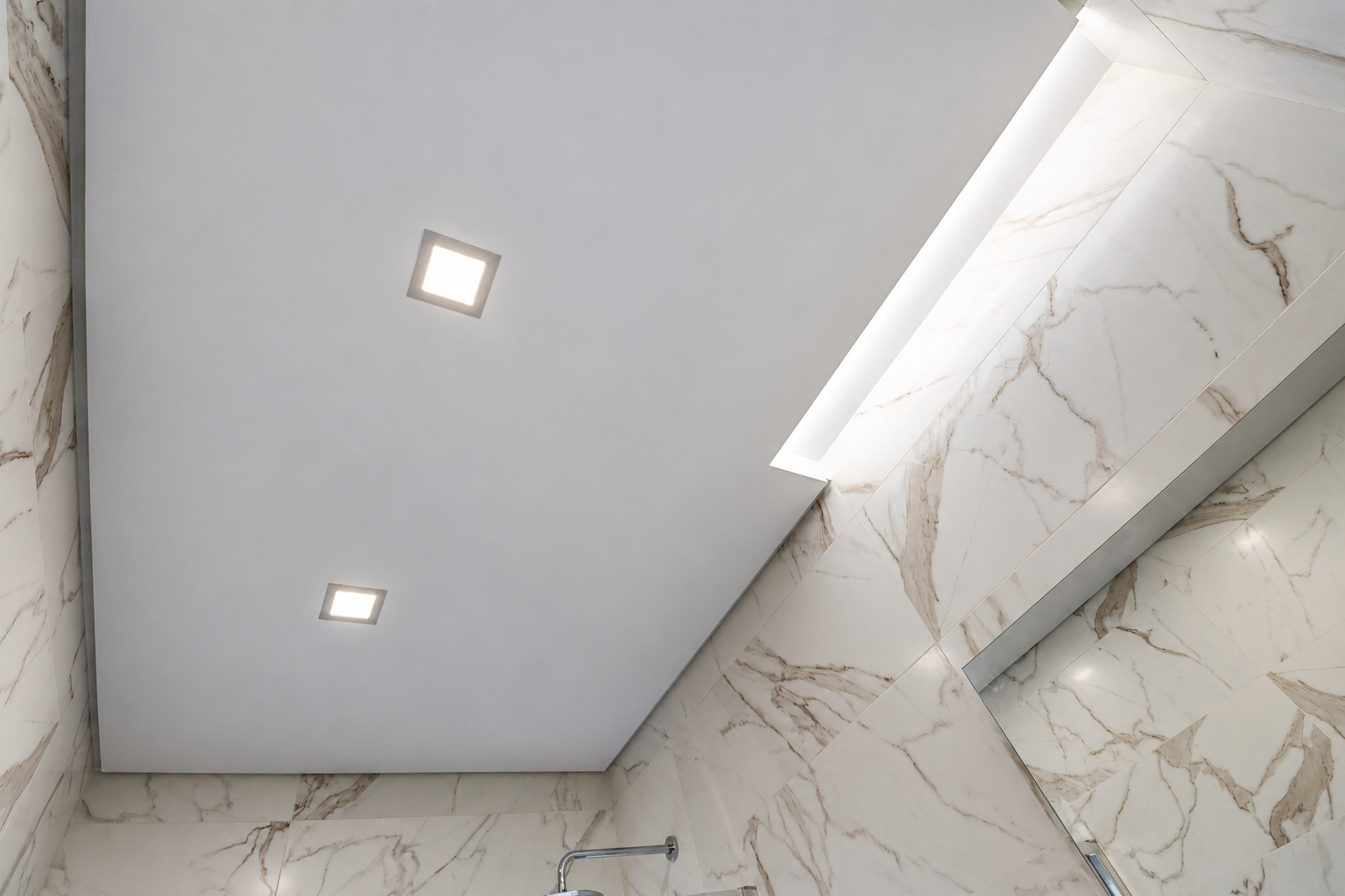 White ceiling with two square spotlights and indirect lighting, between Calacatta-effect walls.