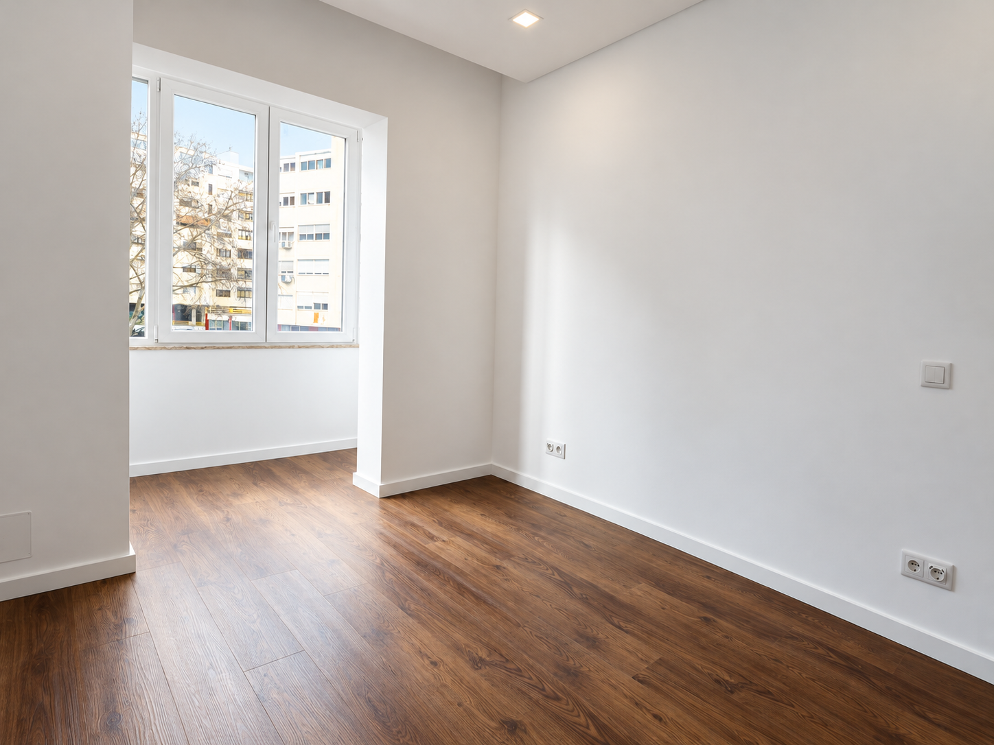 Empty bedroom with a white-framed window, light walls and wood-effect flooring.