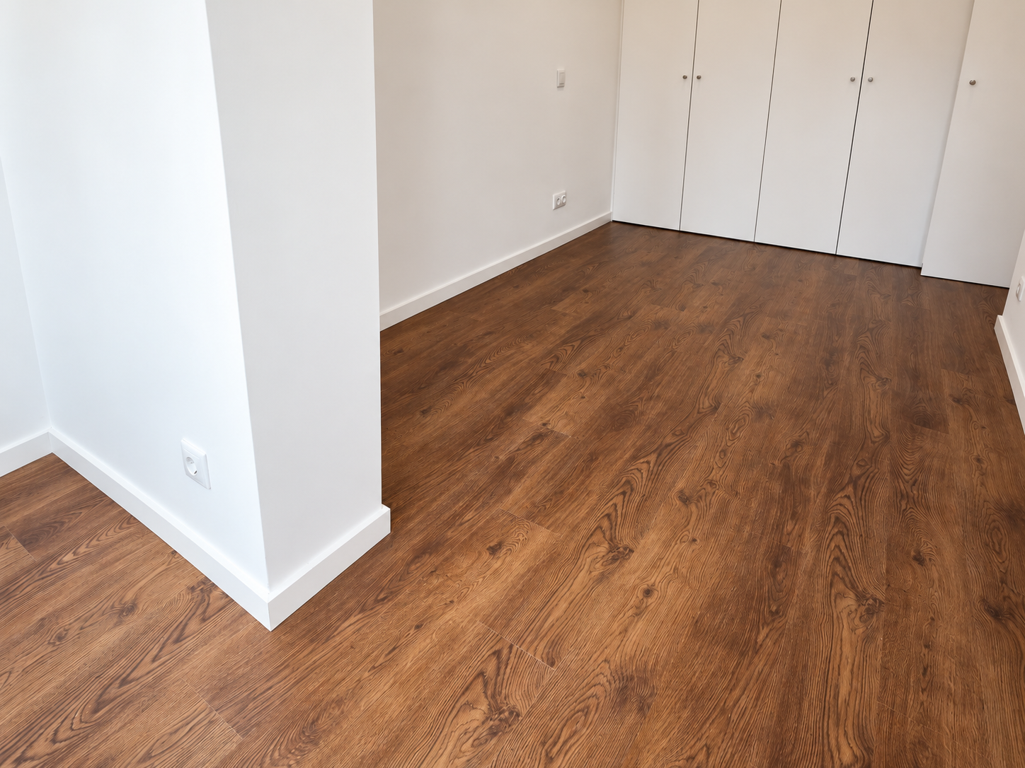 Detail of the wood-effect flooring beside a white wall and the bedroom wardrobe.