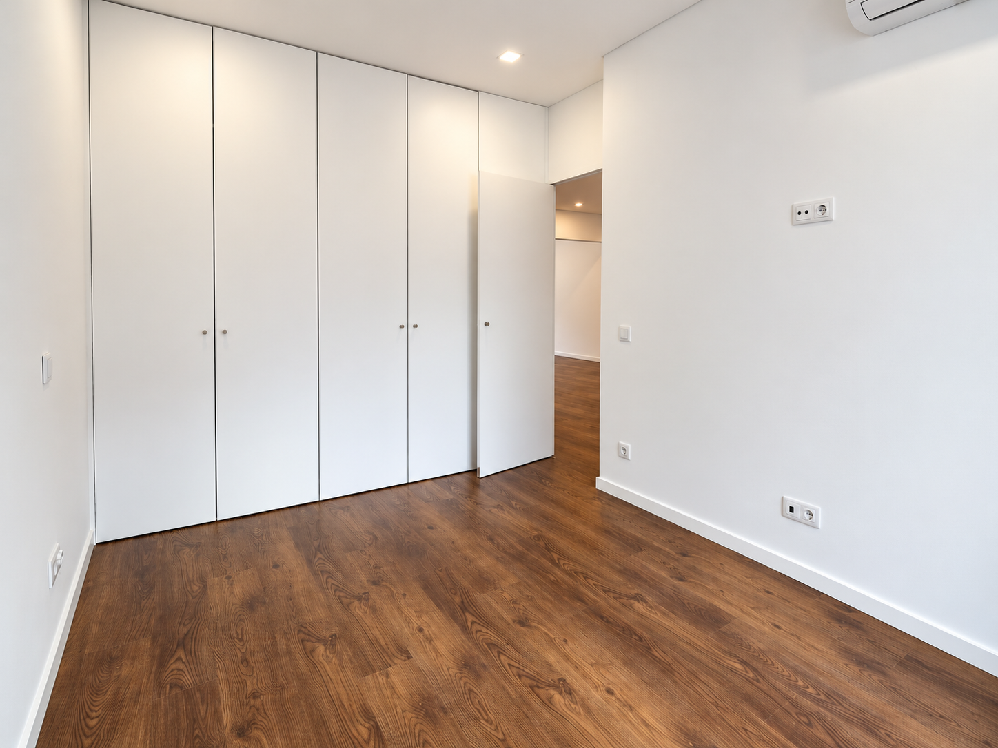 Bedroom with a full-height white wardrobe, an ajar door and wood-effect flooring.