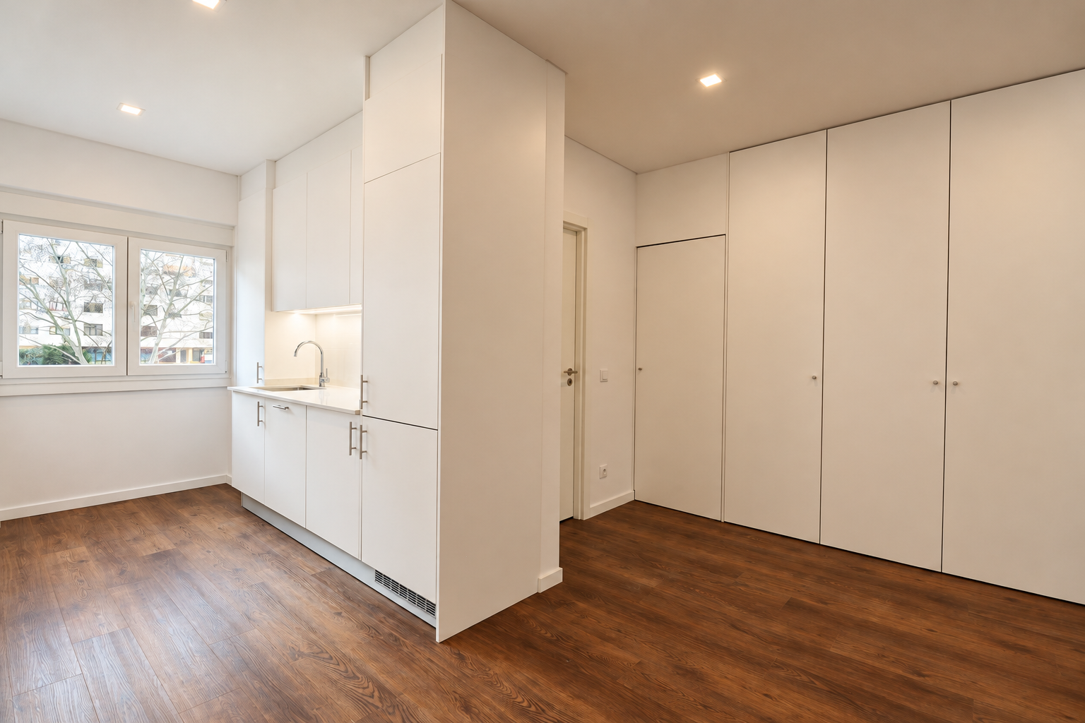 Sink beneath white cupboards beside the window, with a storage unit on the right and wood-effect flooring.