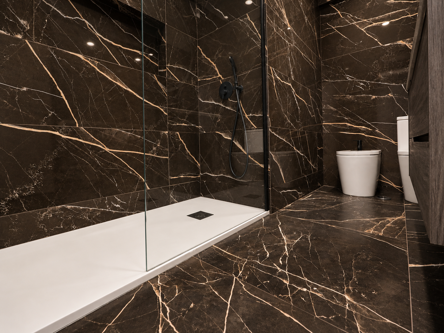 White shower tray and glass screen beside dark wall finishes with light veining